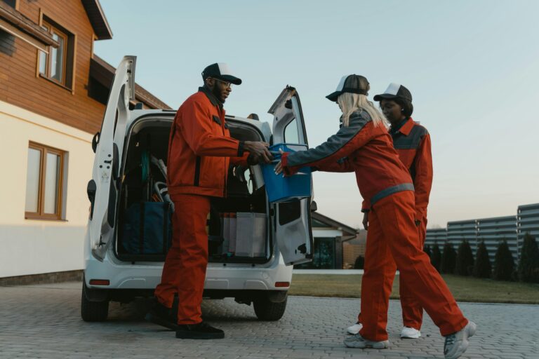 Three adults in uniform unloading equipment from a van outdoors.